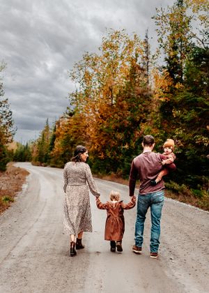 Family walking hand in hand down a scenic autumn road surrounded by colorful trees.