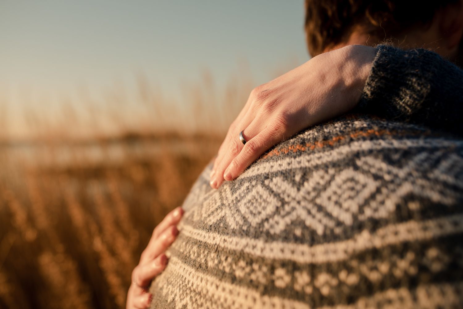 Close-up detail of a Nordic pattern sweater with hands resting on shoulders.