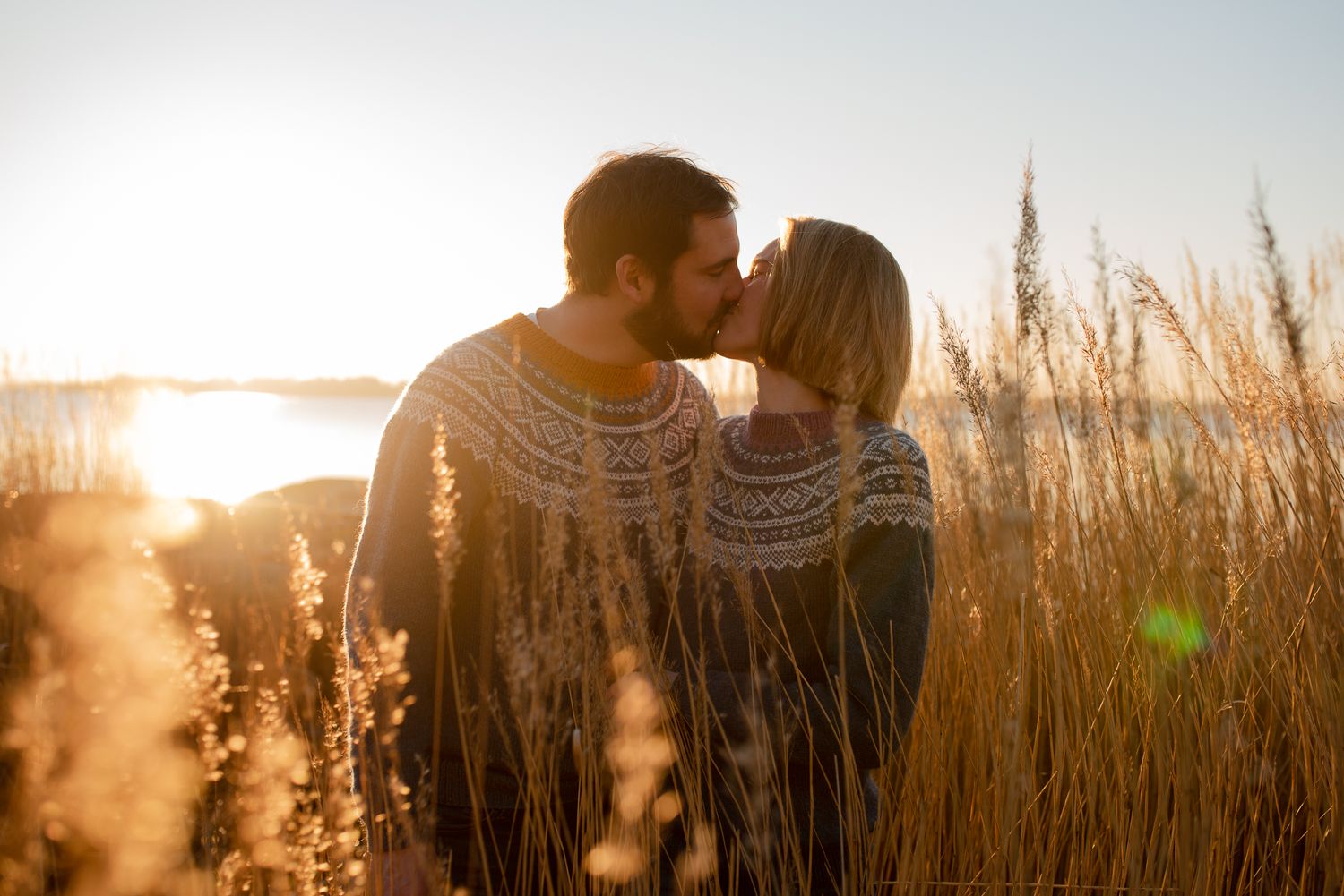 A romantic sunset moment between two people in matching sweaters among golden reeds.