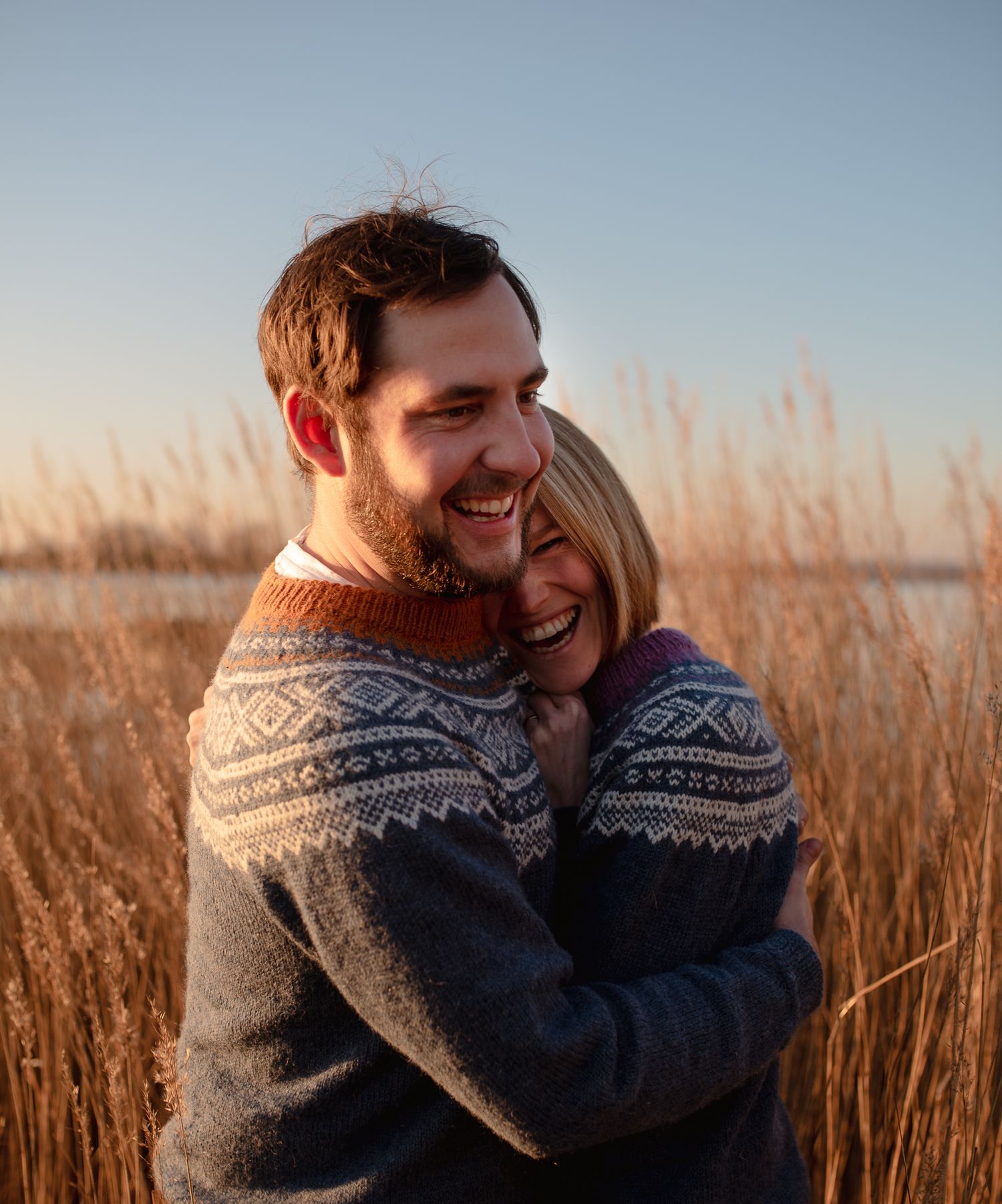 An intimate embrace captured in warm sunlight amidst tall grass by the water.