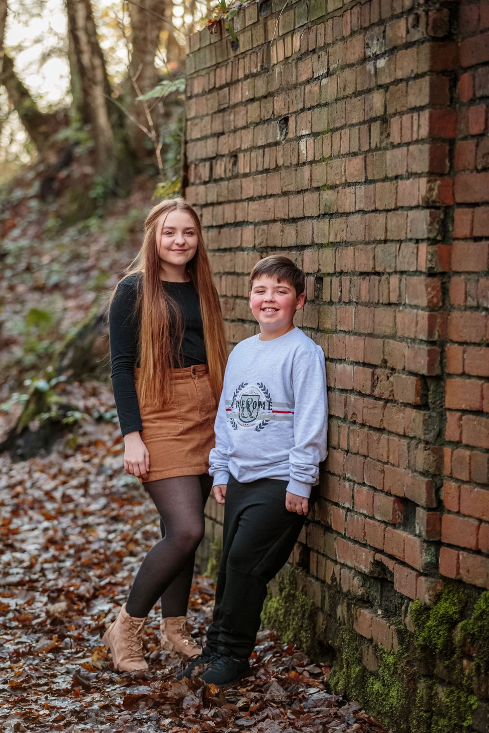 portrait of a young girl and boy leaning against a brick wall