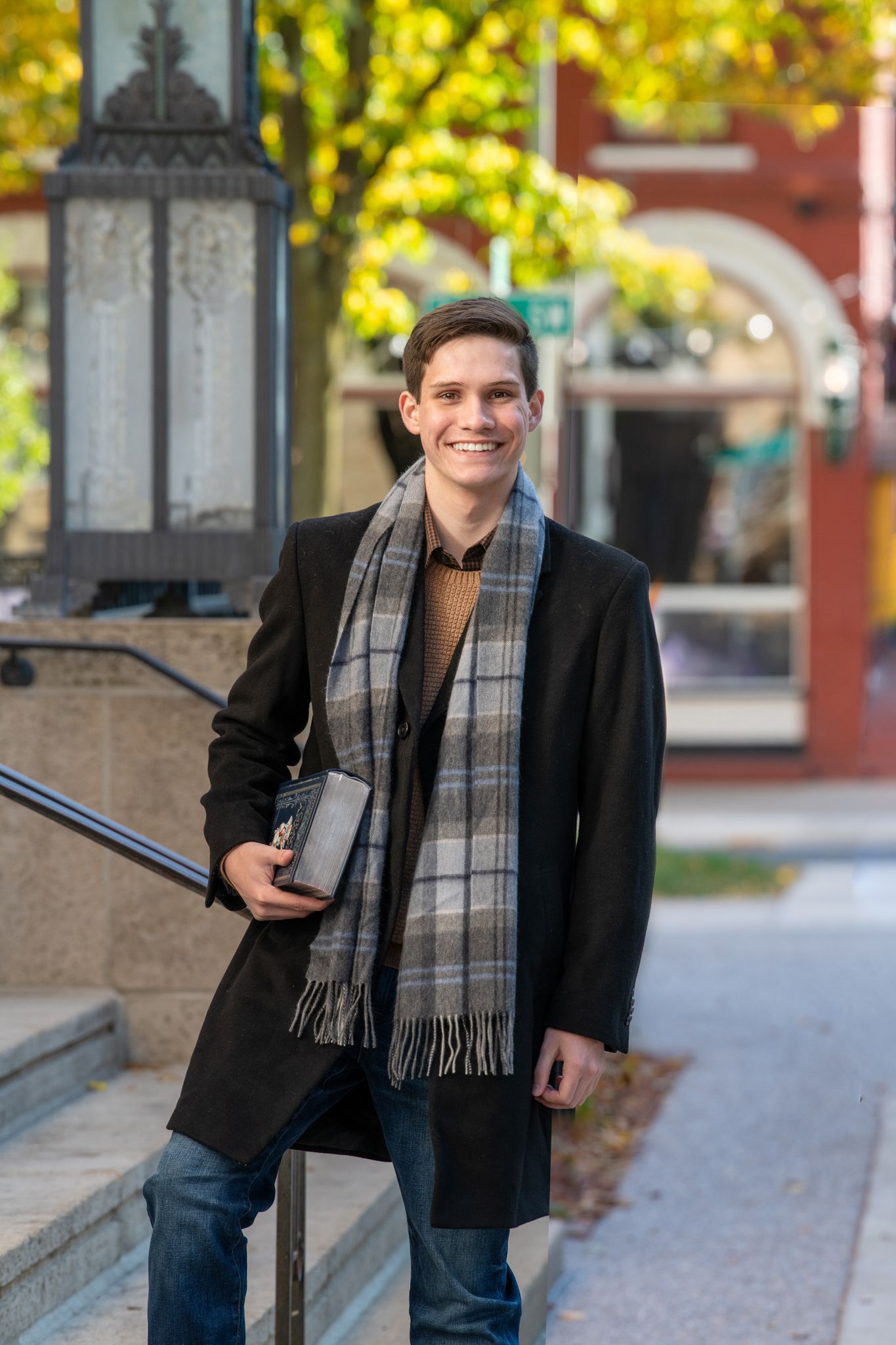Senior boy posing in downtown with cityscape and fall leaves in background.