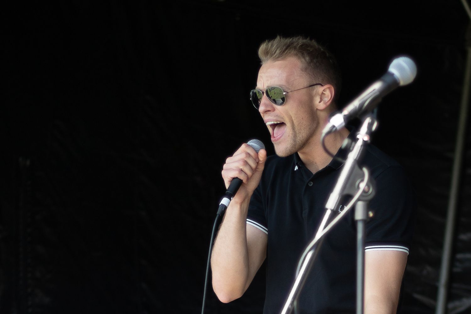 Front man on stage at a concert singing with microphone stand in the foreground
