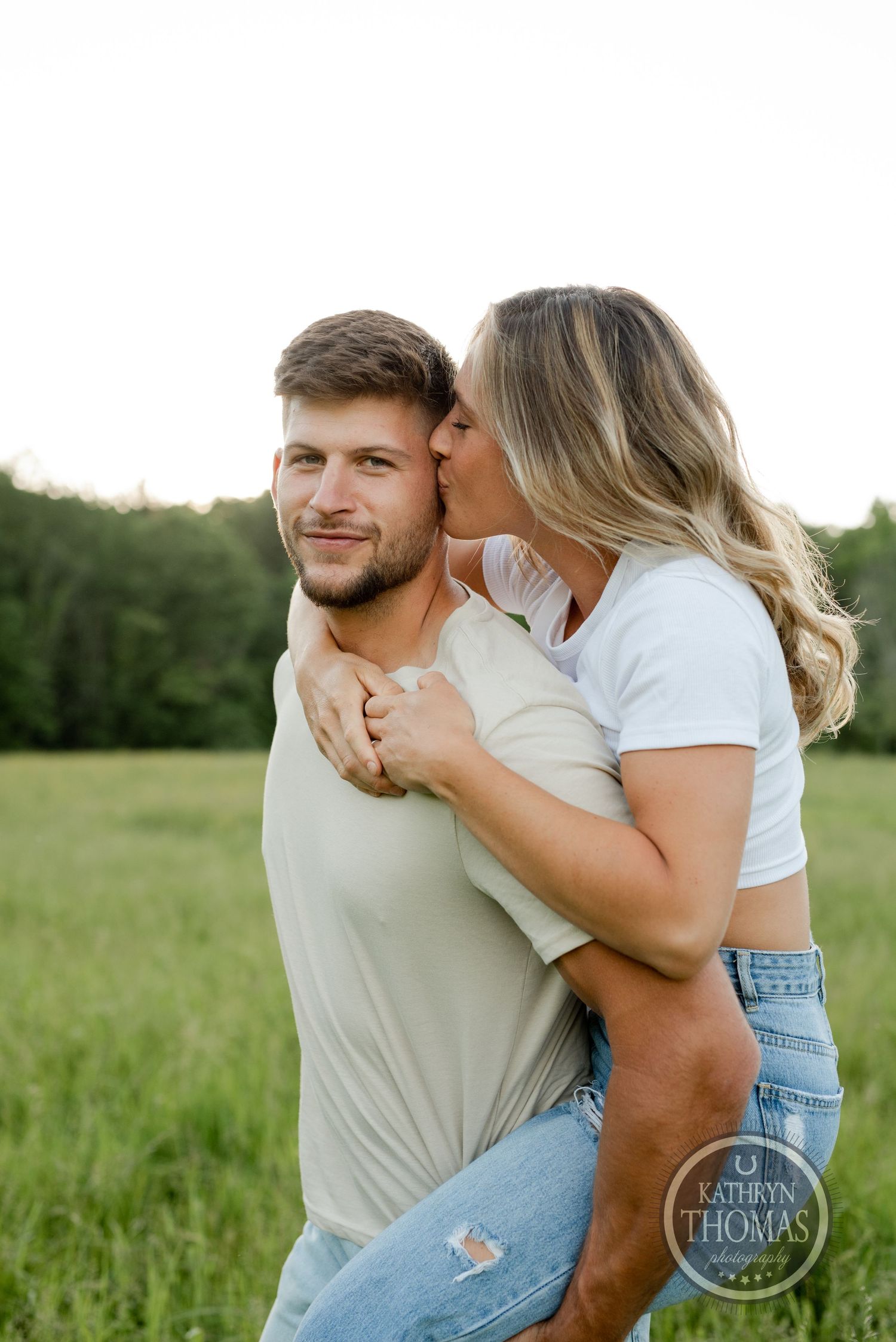 Intimate piggyback portrait in sunlit meadow with natural backdrop.