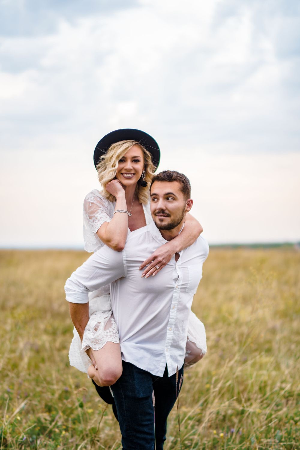 Playful couple in white clothing posing together in a grassy field.