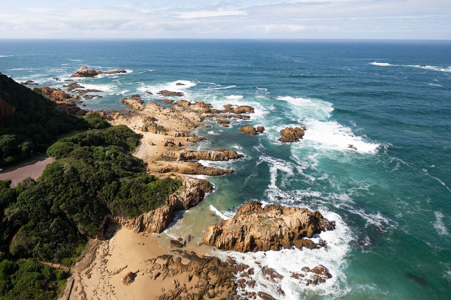 Rocky coastal landscape with crashing waves and rugged cliffs against blue ocean.