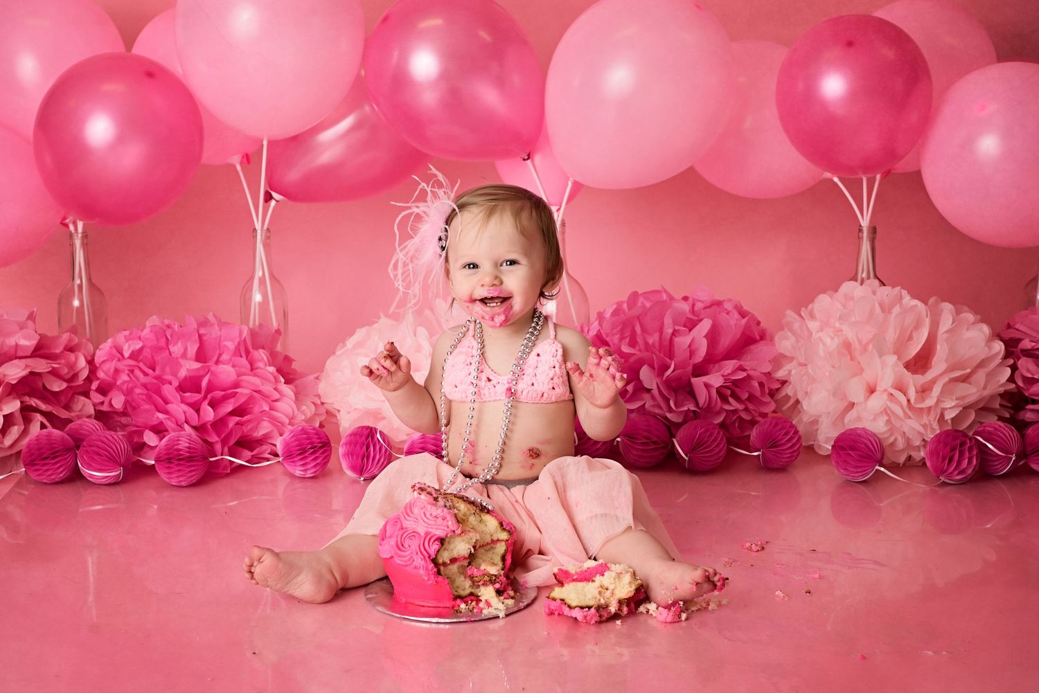 Pink cake smash photography setup with balloons and flowers for first birthday celebration.
