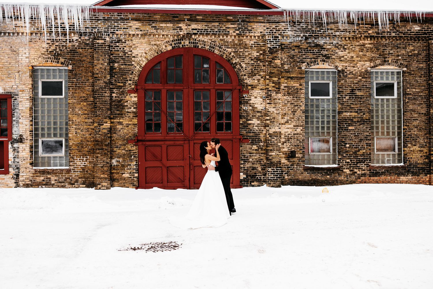 Winter wedding scene with red arched door against stone wall covered in icicles.