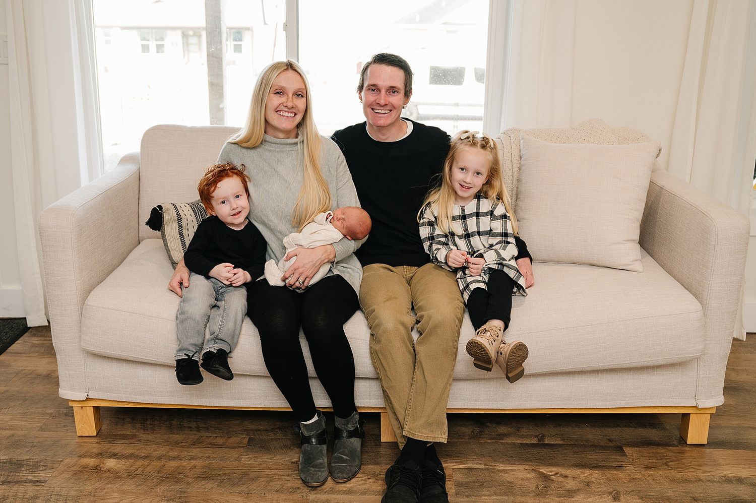 Family portrait of five people sitting together on a light gray couch in a bright living room.