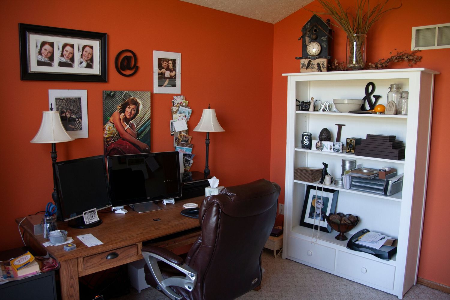 Home office with orange walls decorated with framed photos and artwork.
