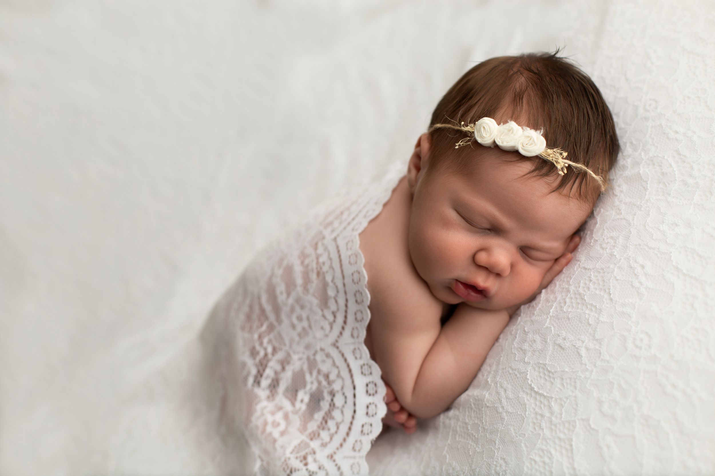 Newborn baby girl laying on lace blanket with her hand under her cheek.