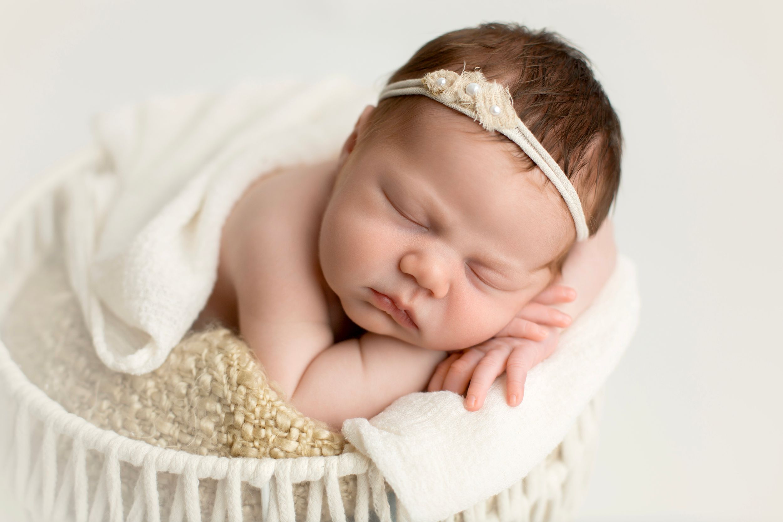Newborn baby girl in a white basket with her hands under her cheek.