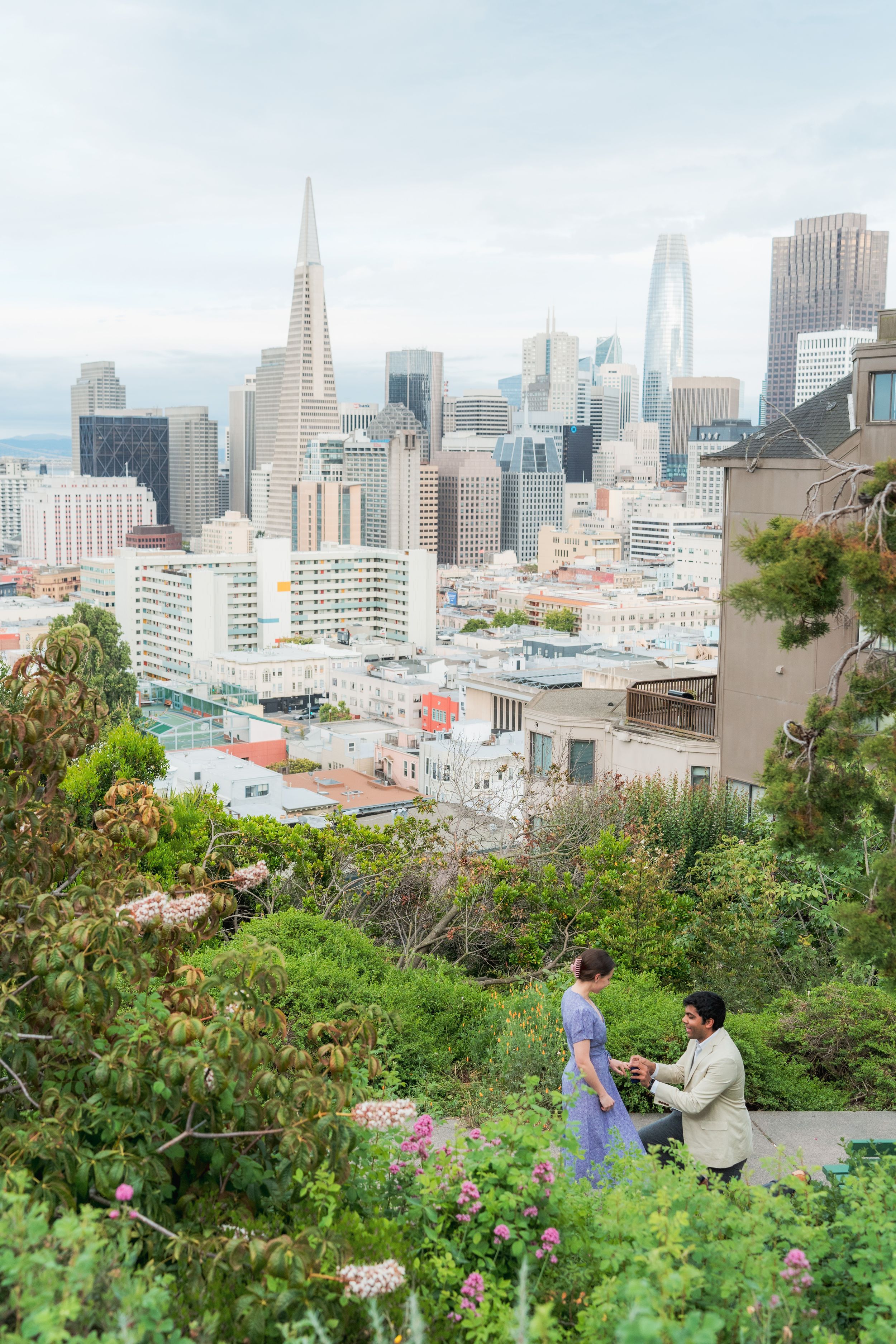 A man proposes to his partner on a hillside garden with the San Francisco skyline in the background.