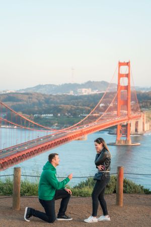 Man proposing on one knee to his partner with the stunning Golden Gate Bridge at sunset.