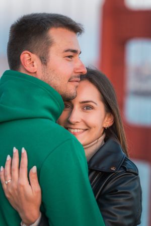 Couple embracing closely near the Golden Gate Bridge, woman smiling warmly at the camera.