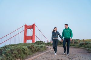 Happy couple walking hand in hand on a path with the Golden Gate Bridge in the background.