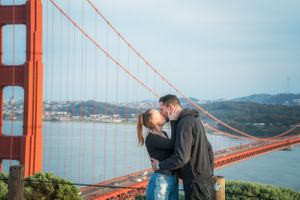 Couple sharing a tender kiss with the majestic Golden Gate Bridge and bay in the background.