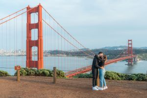 Couple sharing romantic kiss in front of the iconic Golden Gate Bridge in San Francisco.
