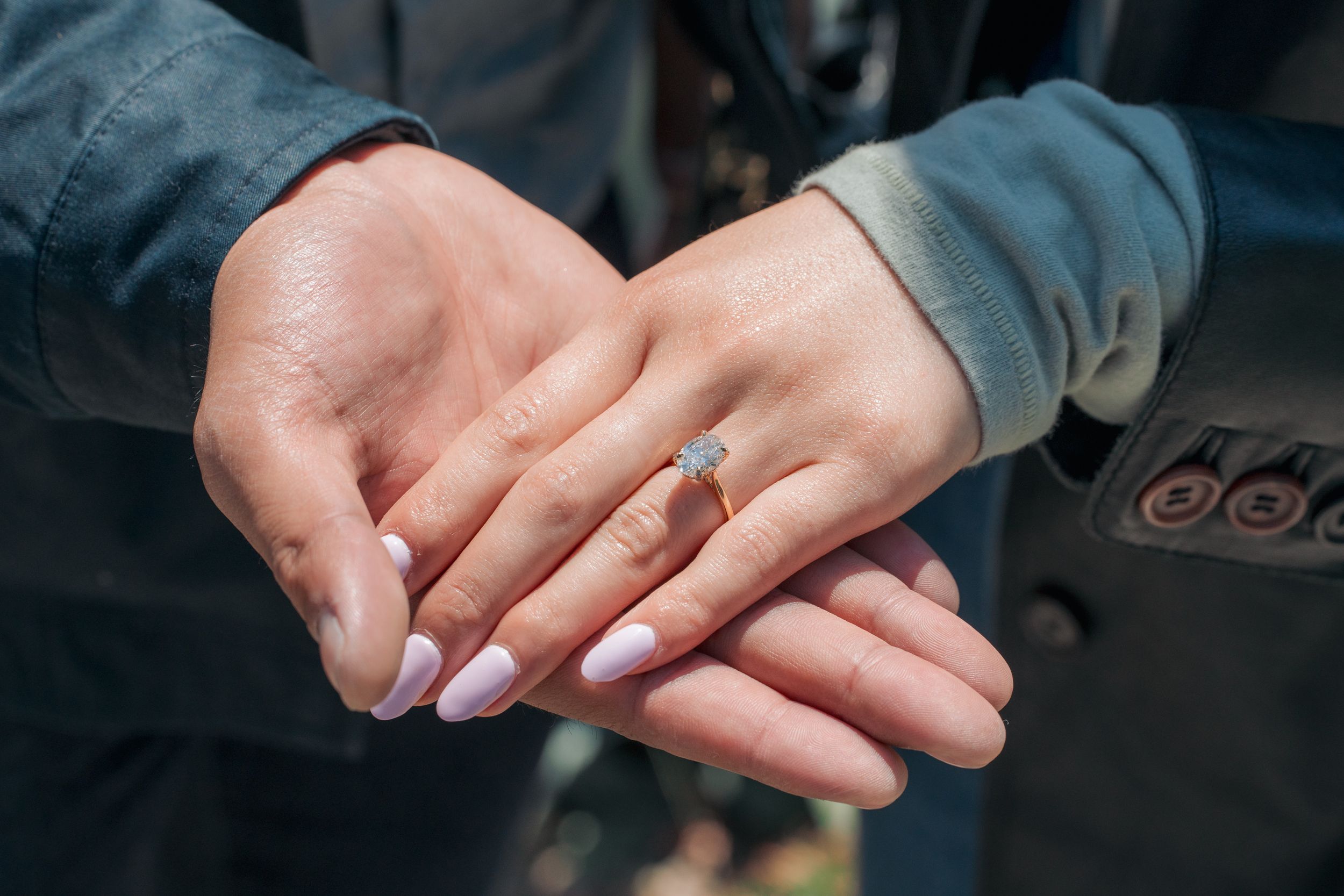 A close-up of two hands together, one wearing a delicate engagement ring with a light blue stone.