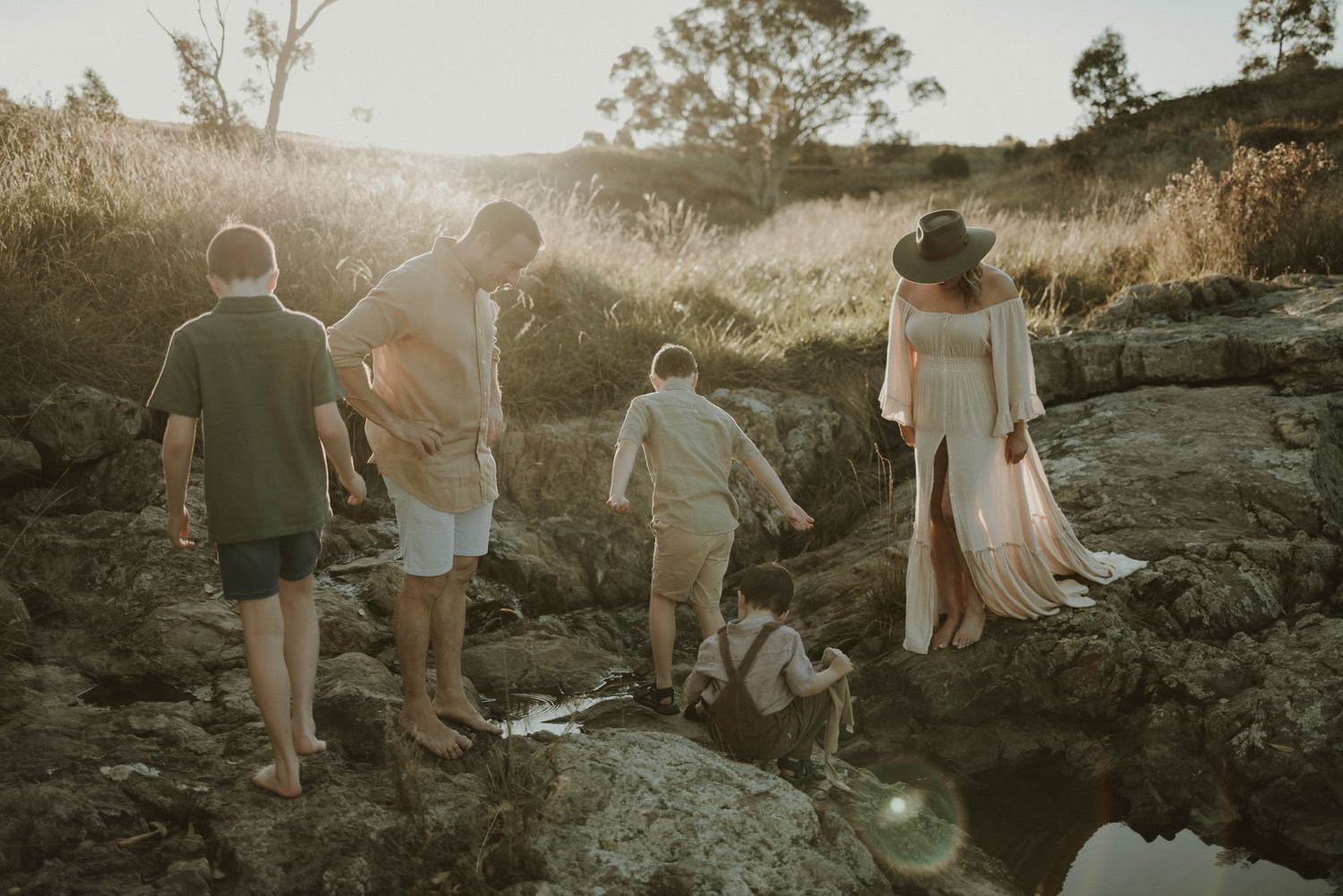 A family walks together on rocky terrain during sunset near the ocean.