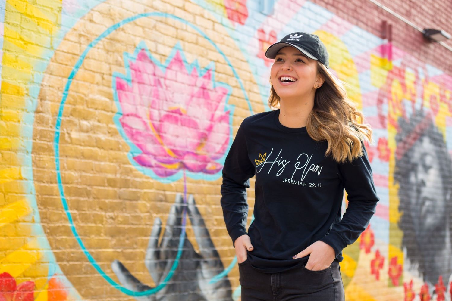 Woman in black sweater smiles near colorful graffiti wall with lotus flower design.
