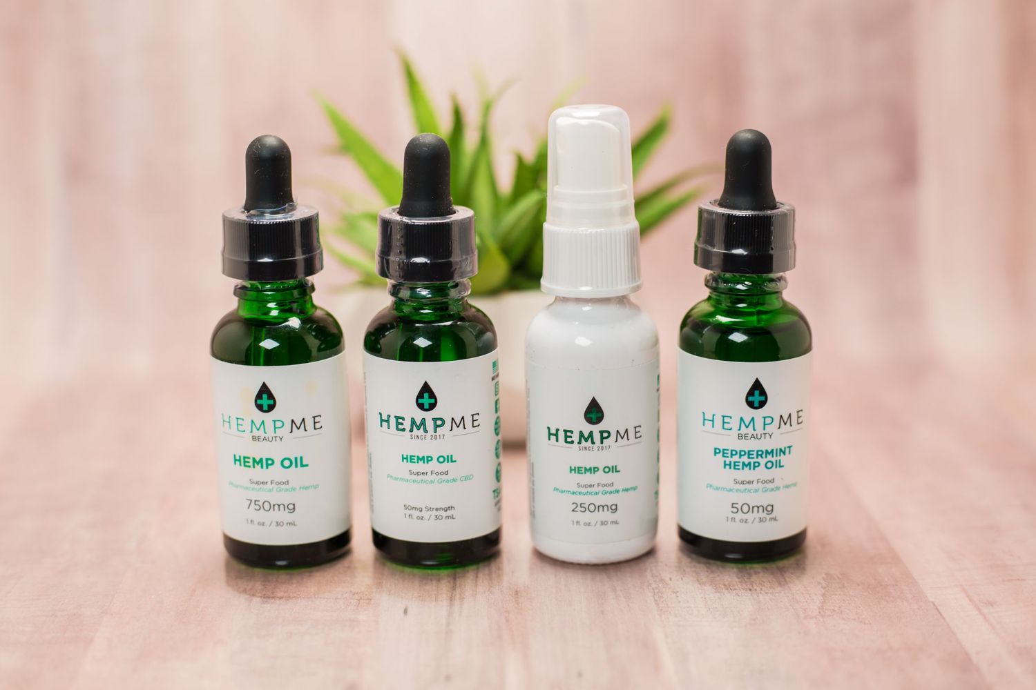 Four green glass dropper bottles of wellness products arranged on wooden surface with plant.