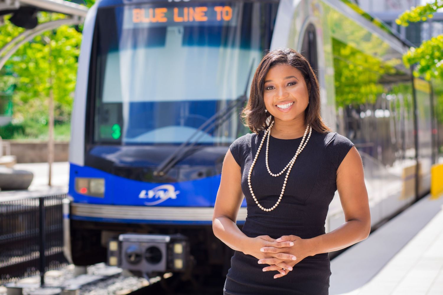 Professional woman in black dress standing in front of public transit bus.