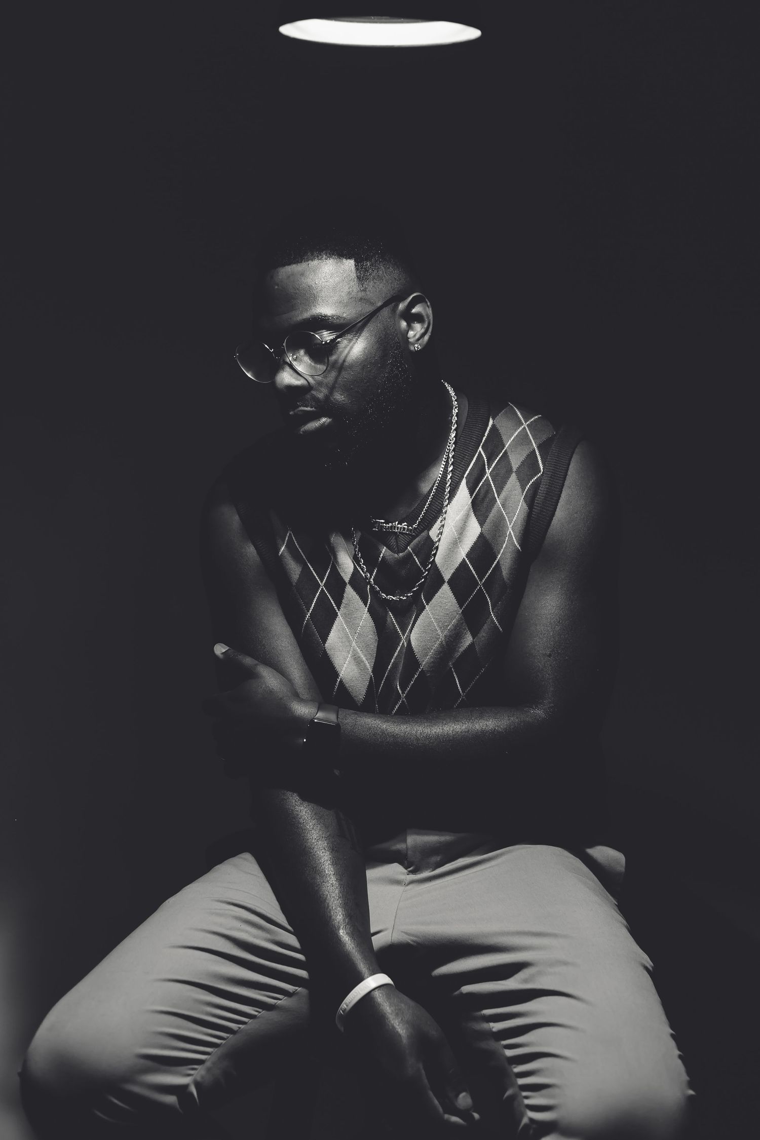 Dramatic black and white portrait of someone in an argyle sweater vest under spotlight.