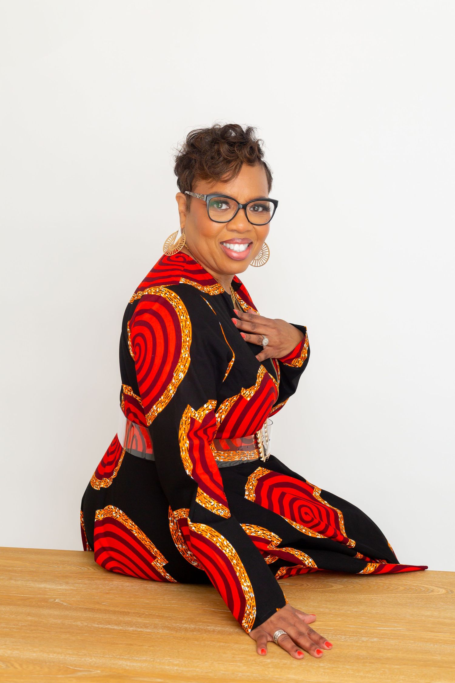 Portrait in vibrant red and black patterned dress sitting on wooden floor.
