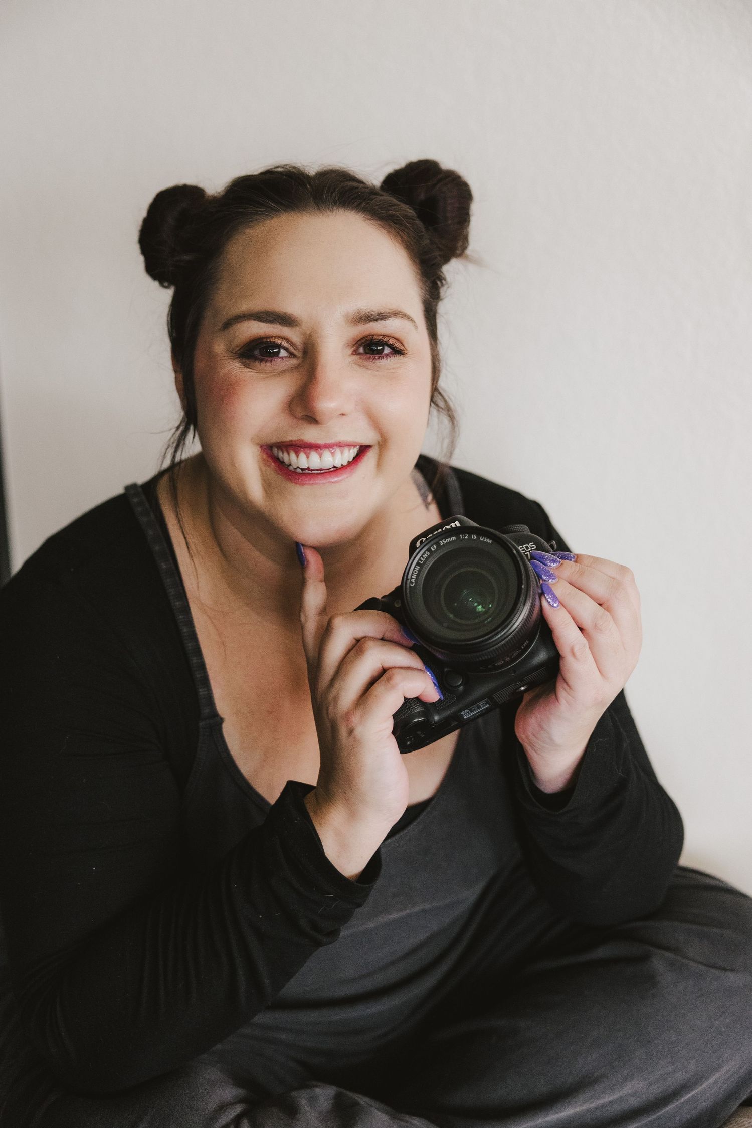 Close-up portrait of photographer with bun hairstyle holding camera against light background. Denver Photographer.