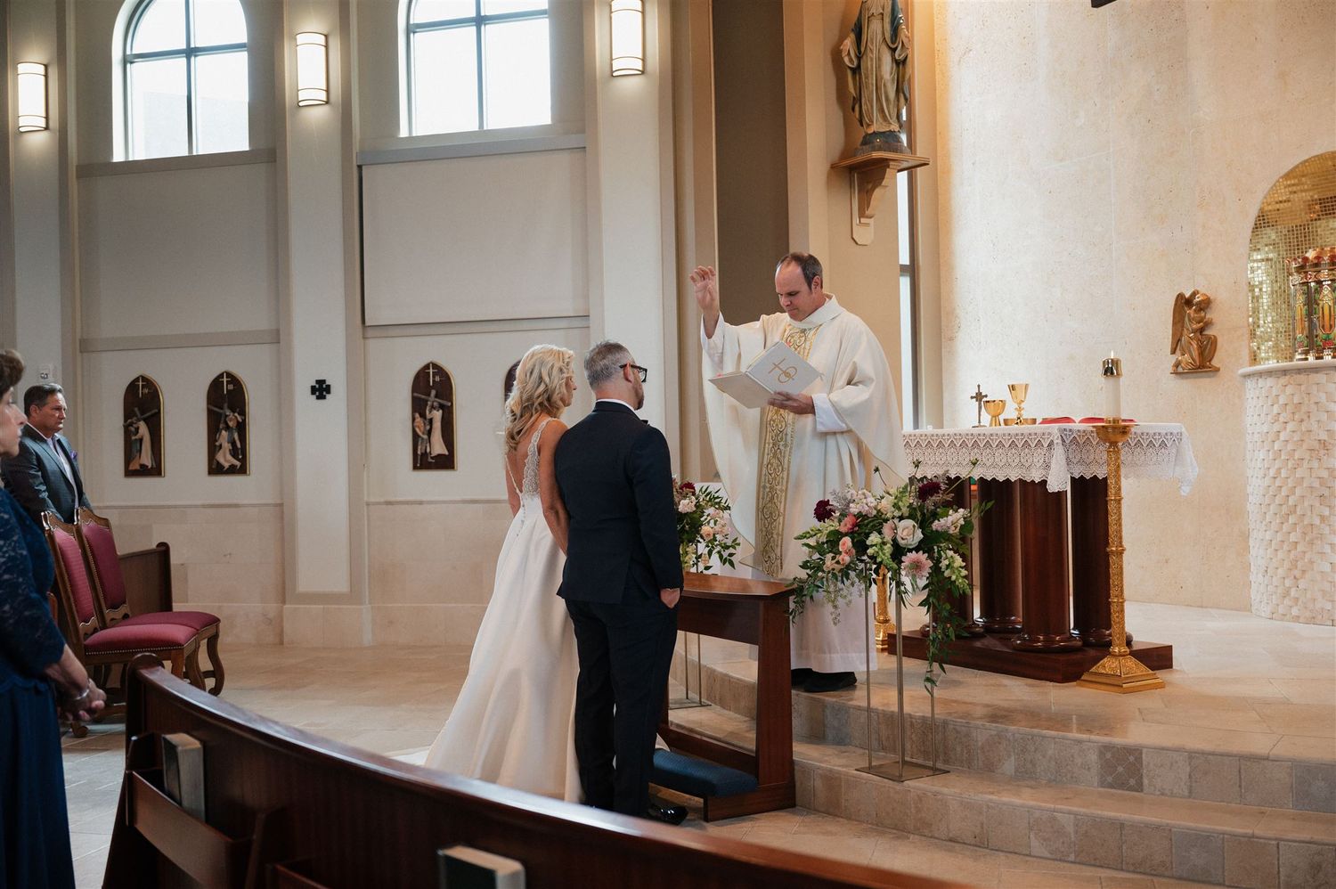 Traditional church wedding ceremony at altar with priest and floral arrangements.