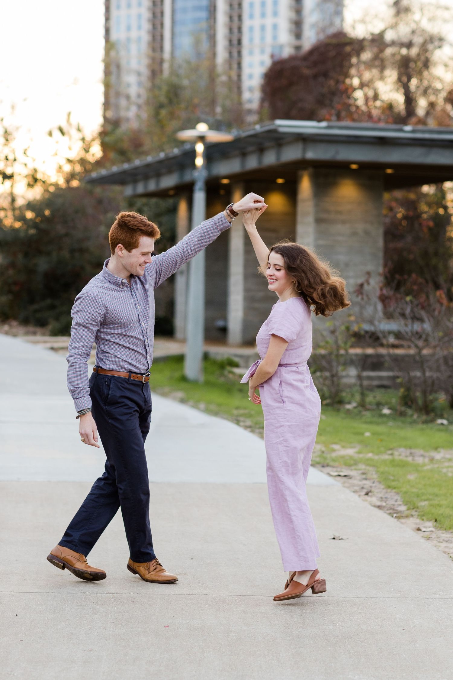 Couple dancing together on a concrete path with tall buildings in background at sunset.