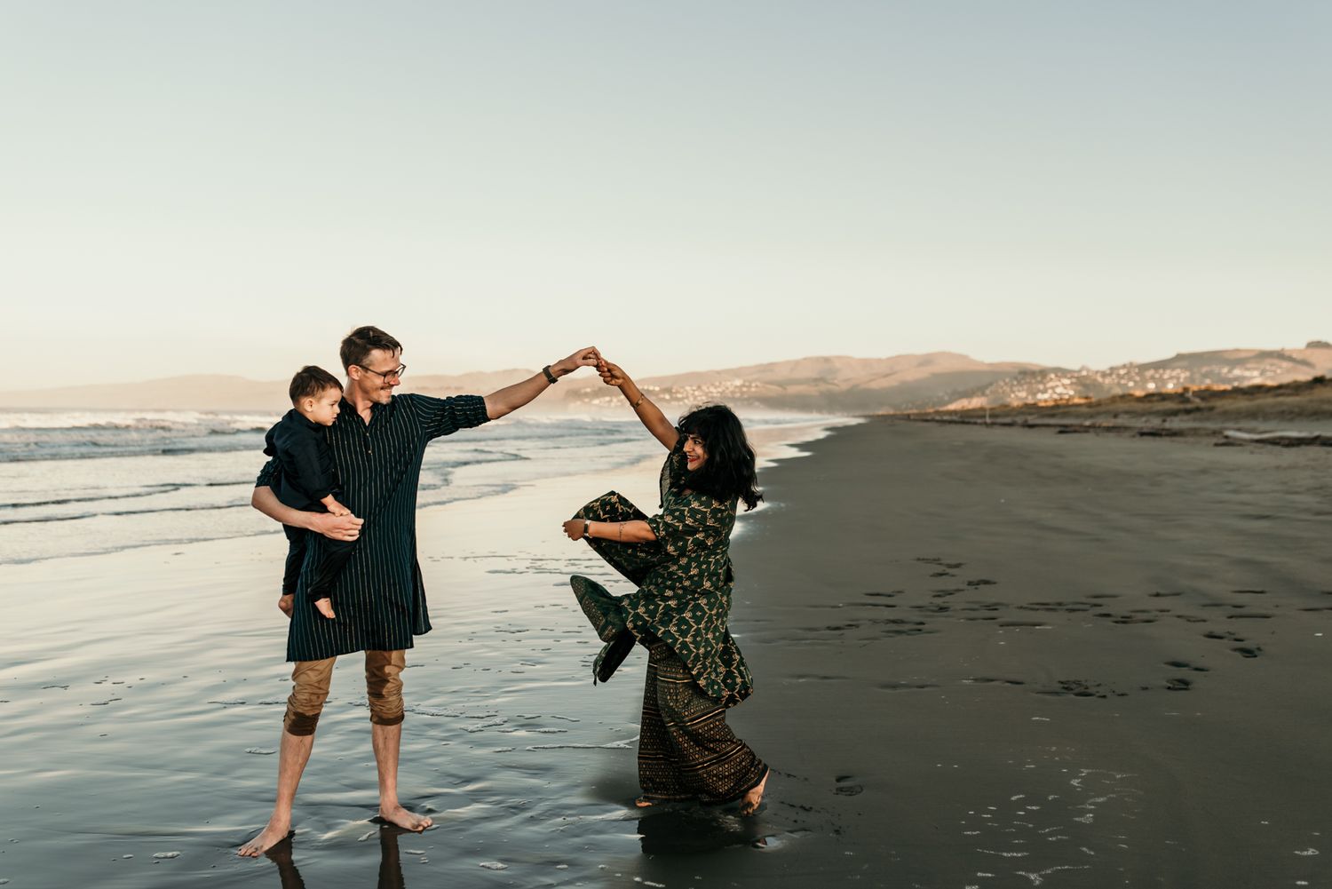 A playful couple dances together at the beach during sunset.