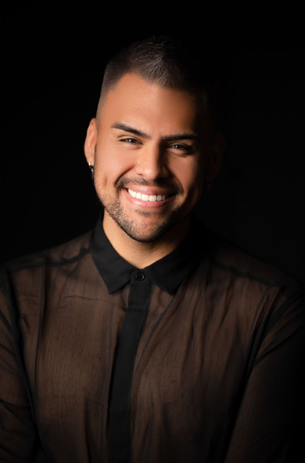 Professional studio portrait of a smiling man in a black shirt against a dark background.