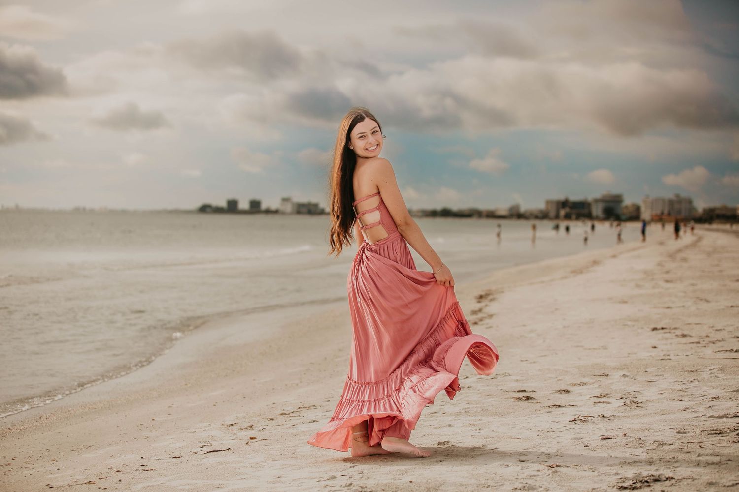 Woman in flowing coral dress twirls on beach at sunset.