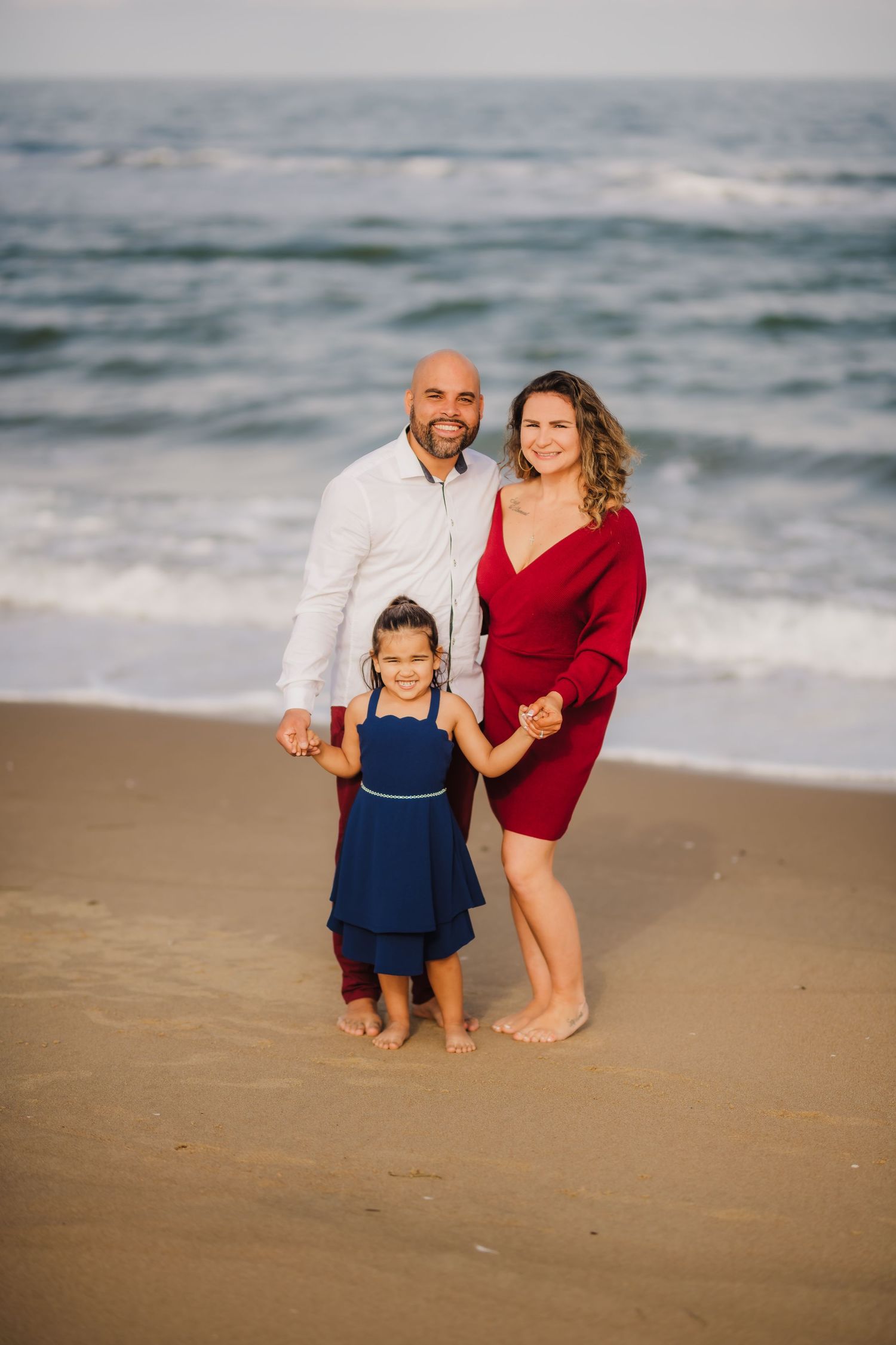 Family portrait on the beach at sunset with ocean waves in the background.