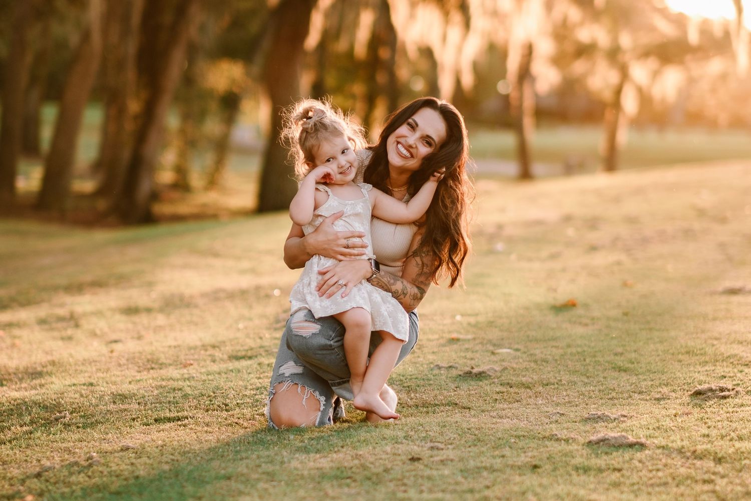 A parent and child share a joyful moment together on a grassy field during golden hour.