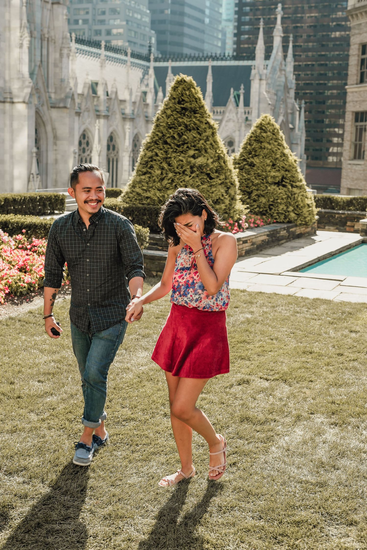 Couple laughing and holding hands on a rooftop garden with St. Patrick's Cathedral spires in the background.
