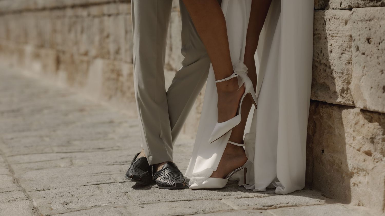 Close-up view of wedding dress details and shoes against a stone wall background.