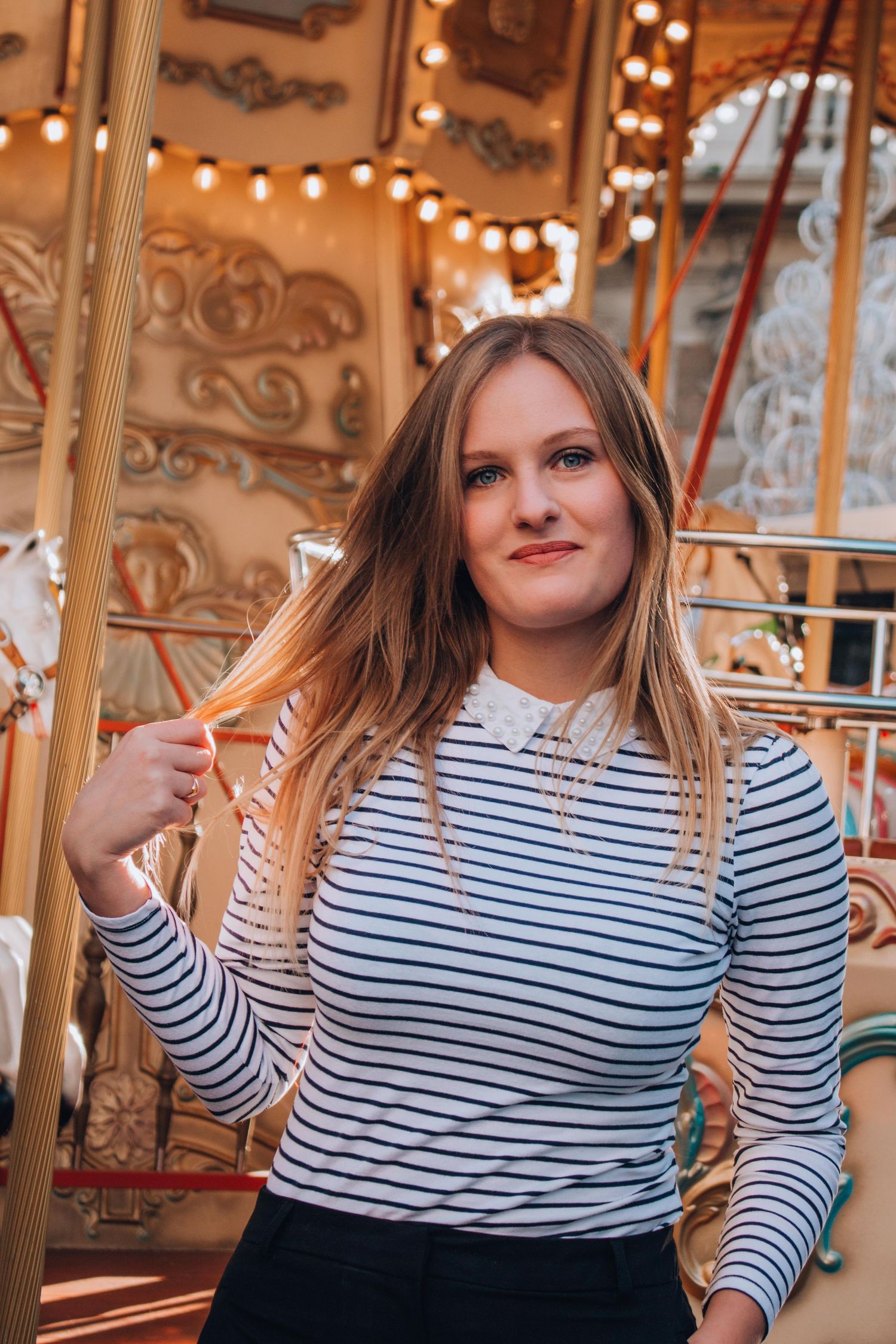 Portrait at carnival carousel with striped shirt and warm lighting.