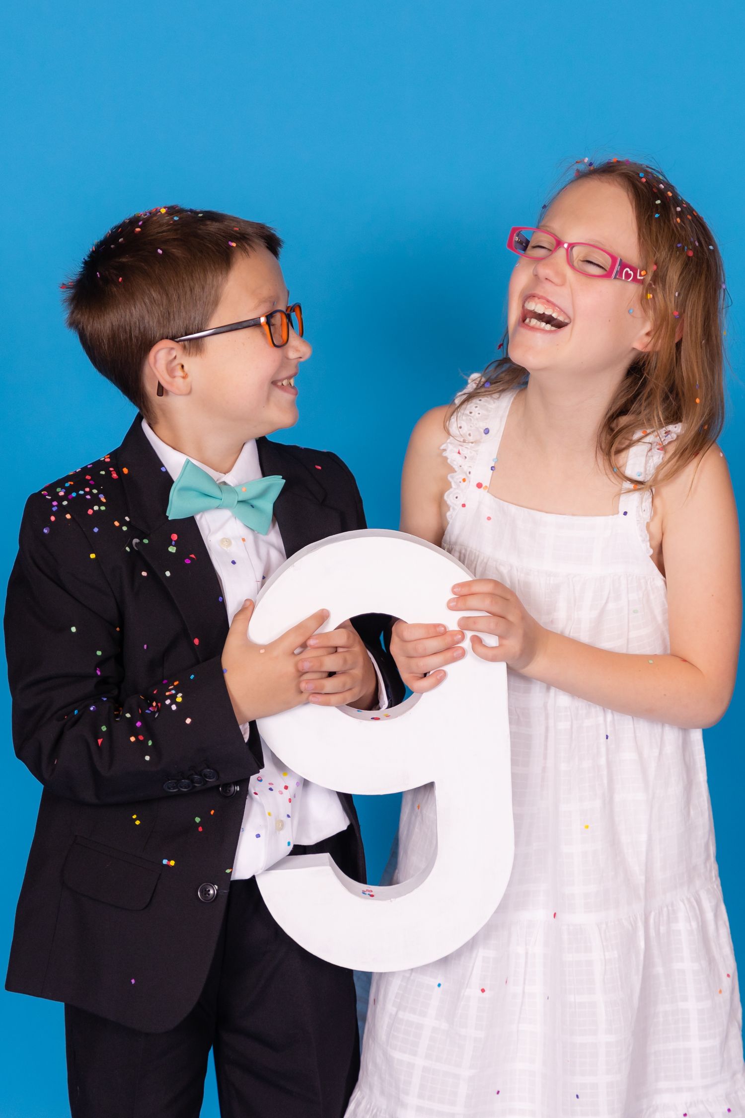 two children holding large 9 and laughing on savage blue jay backdrop with confetti in studio in clayton new jersey