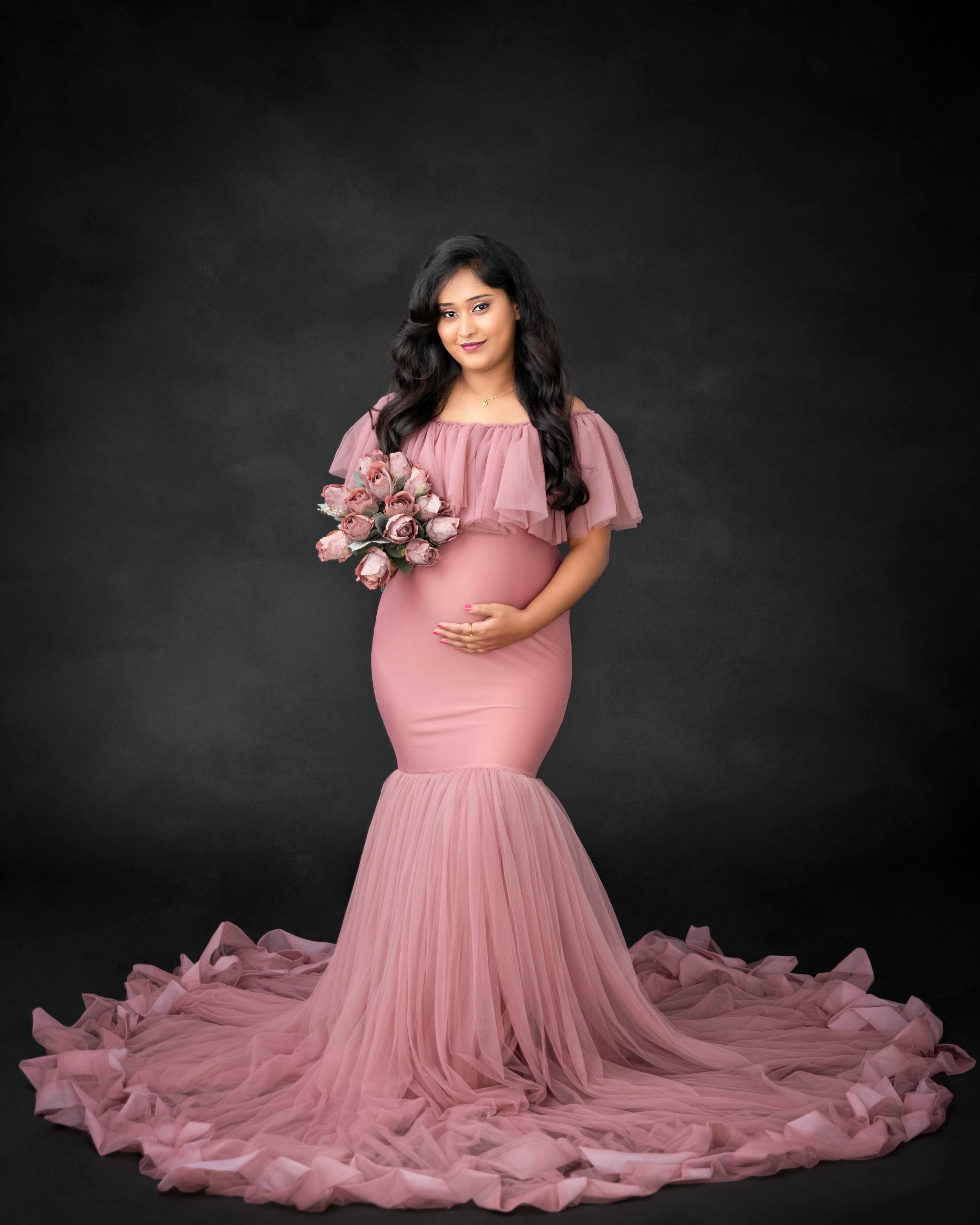 Romantic maternity portrait in pink mermaid gown holding bouquet with flowing train.