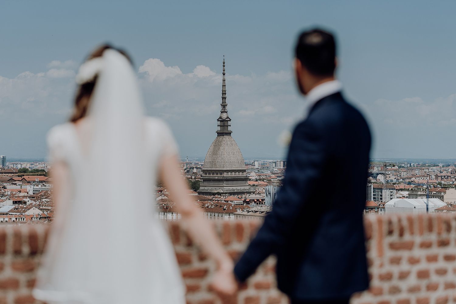 Bride and groom hold hands with iconic Mole Antonelliana tower of Turin in background.