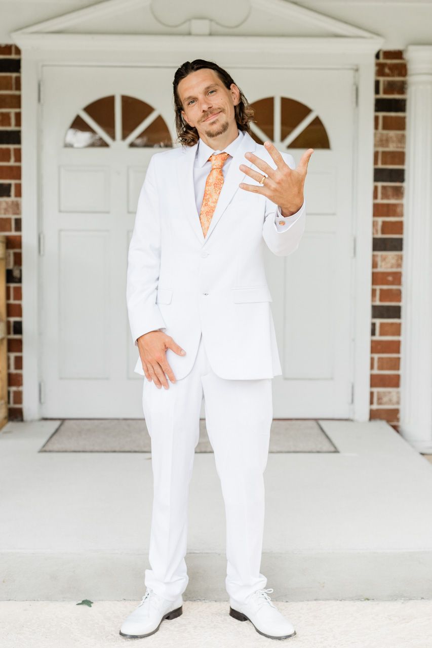 A person wearing an all-white outfit poses in front of white garage doors.
