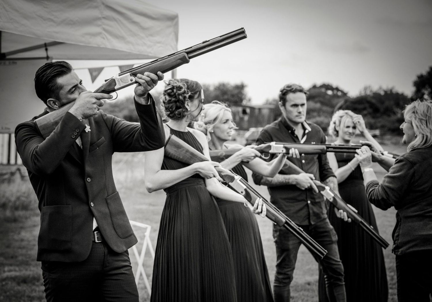 Wedding party holding clay shooting rifles in formal attire.