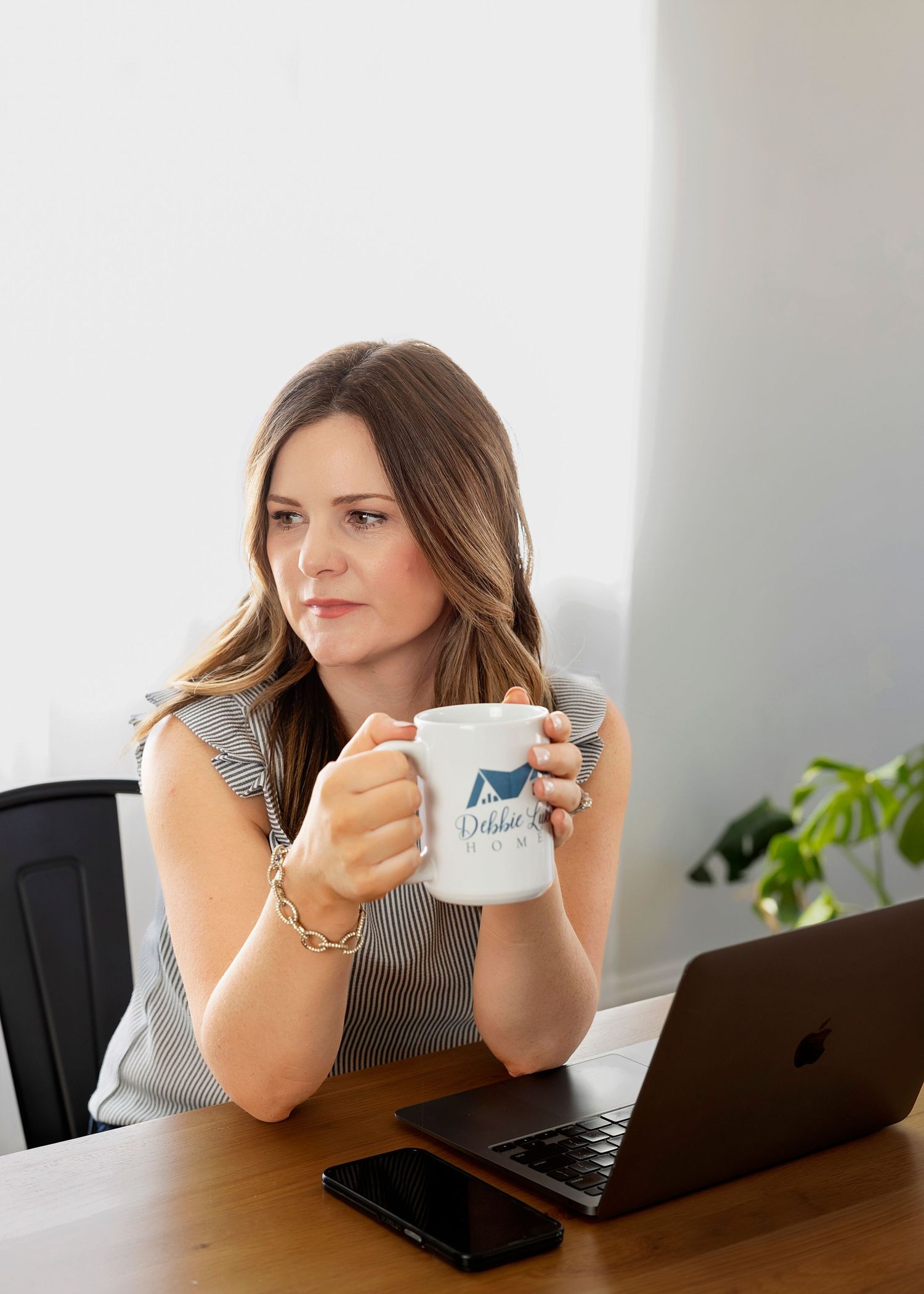 Person holding coffee mug while working at desk with laptop in office setting.