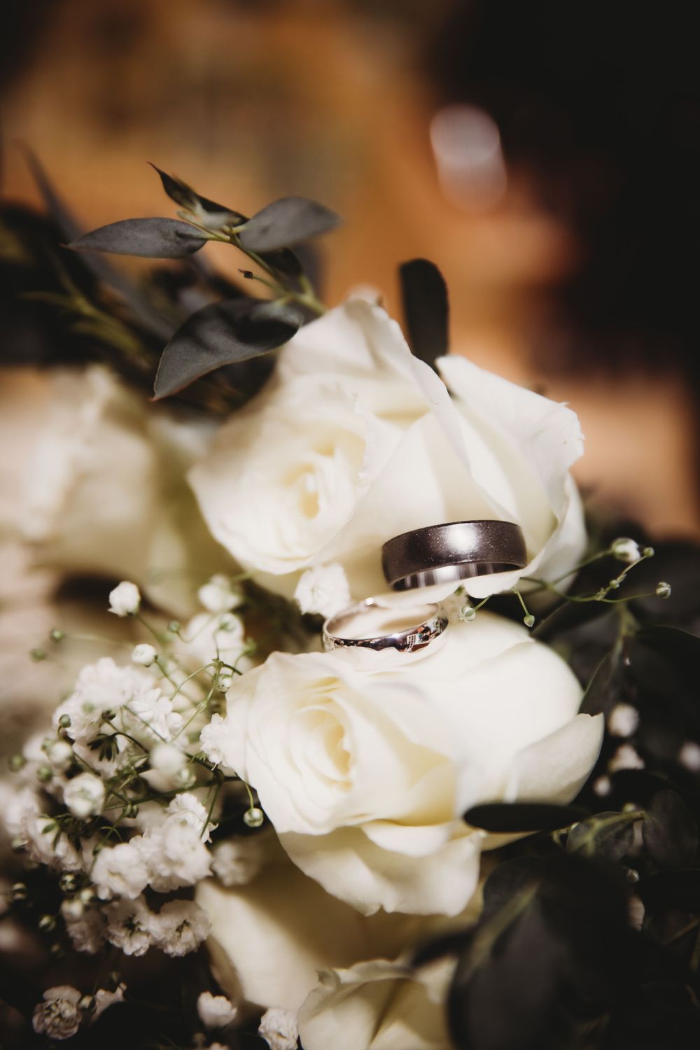 Wedding rings nestled among white roses and baby's breath in a romantic detail shot.