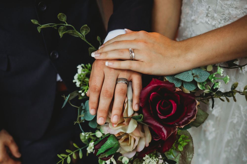 Close-up of wedding rings and hands on red and white floral bouquet.