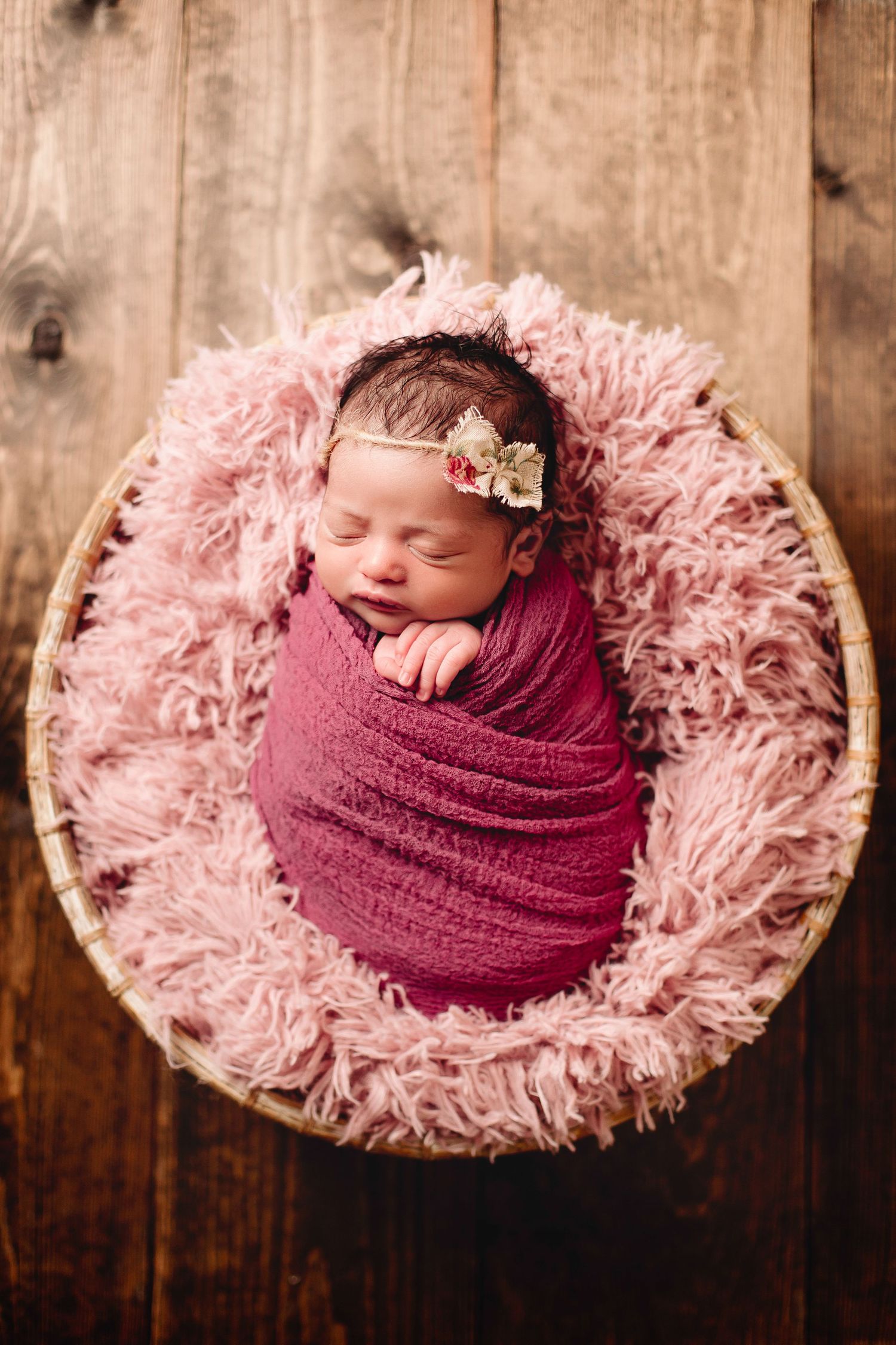baby wrapped in pink sleeping in basket stuffed with pink fur