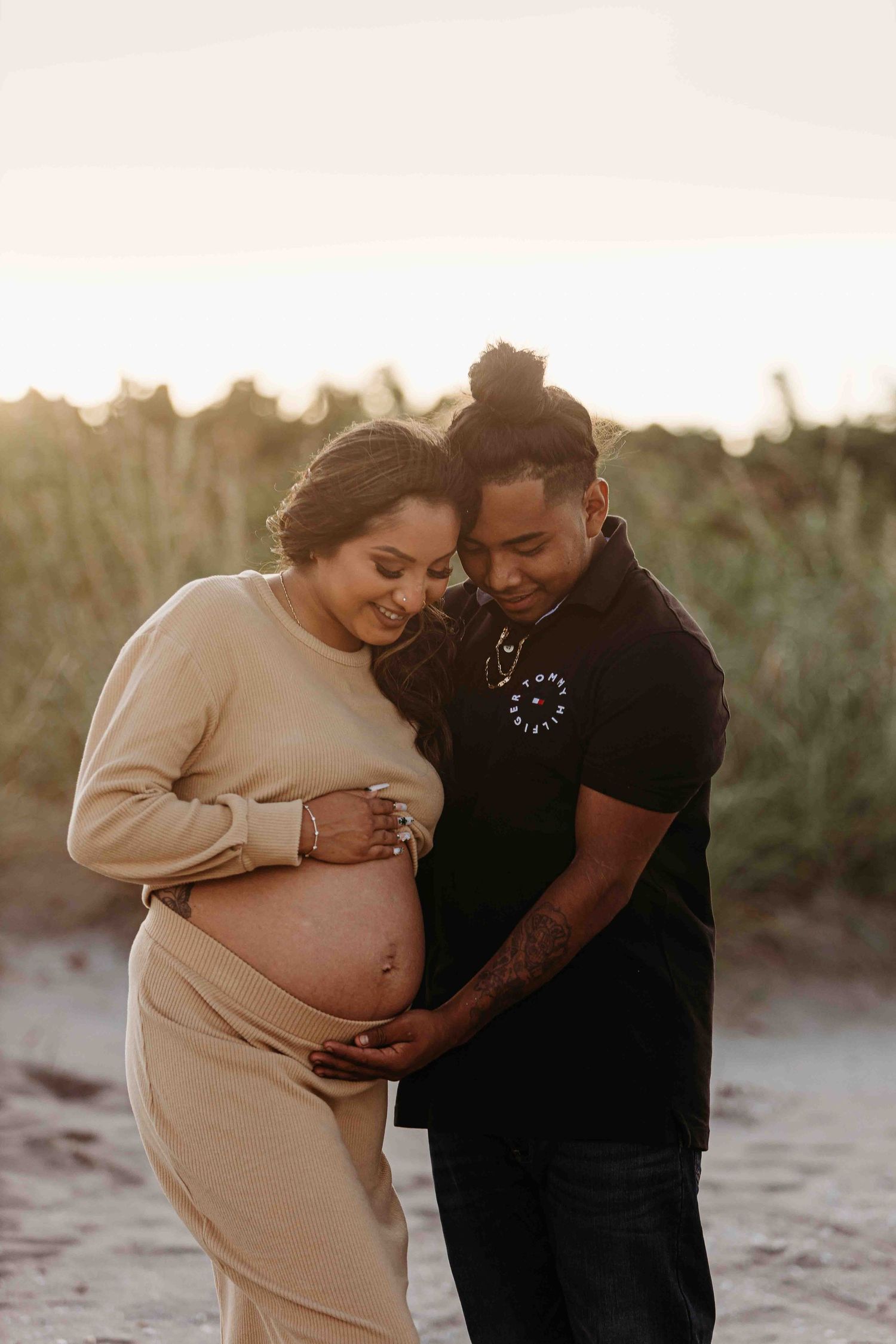 Intimate maternity photo of couple embracing on beach at sunset.